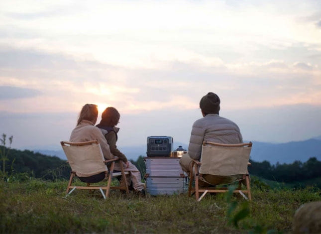 Familie sitzt mit Campingstühlen und schaut Sonnenuntergang, auf Tisch steht Powerstation von Ecoflow