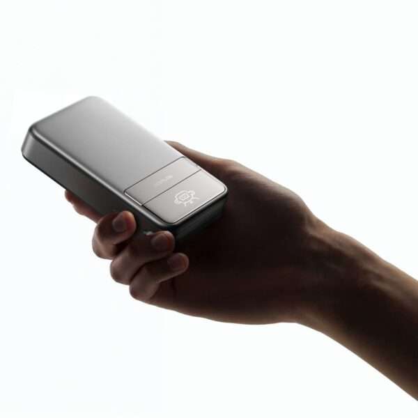 Ein schlankes, metallisch graues Handheld-Gerät wird in der Hand einer Person vor einem hellen, weißen Hintergrund gezeigt. Das Gerät hat ein glattes, rechteckiges Design mit einer minimalistischen Taste und einem Symbol auf der Oberfläche, was auf fortschrittliche Technologie hindeutet. Die Hand, die das Gerät hält, hat einen neutralen Hautton, der den Kontrast zur polierten Oberfläche des Geräts hervorhebt.
