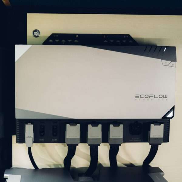 Es wird ein schlanker, moderner EcoFlow Power Hub gezeigt, der ein metallisch-graues Gehäuse mit kantigen Designelementen aufweist. Der obere Teil hat eine glänzende Oberfläche, während der untere Teil mehrere Anschlüsse für Eingangs- und Ausgangsverbindungen hat. Schwarze und graue Kabel sind mit dem Hub verbunden und sorgen für ein aufgeräumtes Erscheinungsbild. Das Produkt ist auf einer hellen Oberfläche mit einer minimalistischen Ästhetik montiert, die seine Funktionalität für das Energiemanagement hervorhebt.