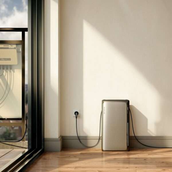 Ein elegantes, modernes Gerät steht vor einer hellen Wand in einer sonnendurchfluteten Ecke eines Raumes. Das Gerät ist metallisch goldfarben und hat ein minimalistisches Design. Es ist mit einem schwarzen Kabel an eine Steckdose angeschlossen. Ein großes Glasfenster in der Nähe bietet einen Blick nach draußen, wobei das Sonnenlicht sanfte Schatten auf den polierten Holzboden wirft und die moderne Ästhetik des Raumes unterstreicht.