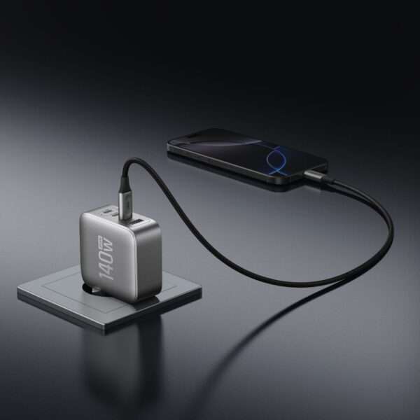 Ein elegantes, silbernes 140-Watt-Netzteil liegt auf einem minimalistischen Ladepad und ist über ein schwarzes, geflochtenes Ladekabel mit einem modernen Smartphone verbunden. Der dunkle Hintergrund hebt die polierten Oberflächen des Ladegeräts und des Telefons hervor und schafft eine anspruchsvolle technische Ästhetik.