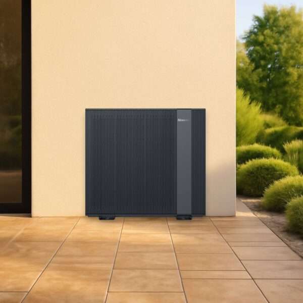 Eine elegante, moderne Wärmepumpe steht an einer glatten, hellen Wand auf einer gefliesten Terrasse. Die Heizung hat ein vertikales Streifendesign in Dunkelgrau mit horizontalen Linien auf der Oberfläche. Im Hintergrund unterstreichen üppiges Grün und eine gepflegte Landschaft die Außenanlage und sorgen für eine ruhige Atmosphäre.
